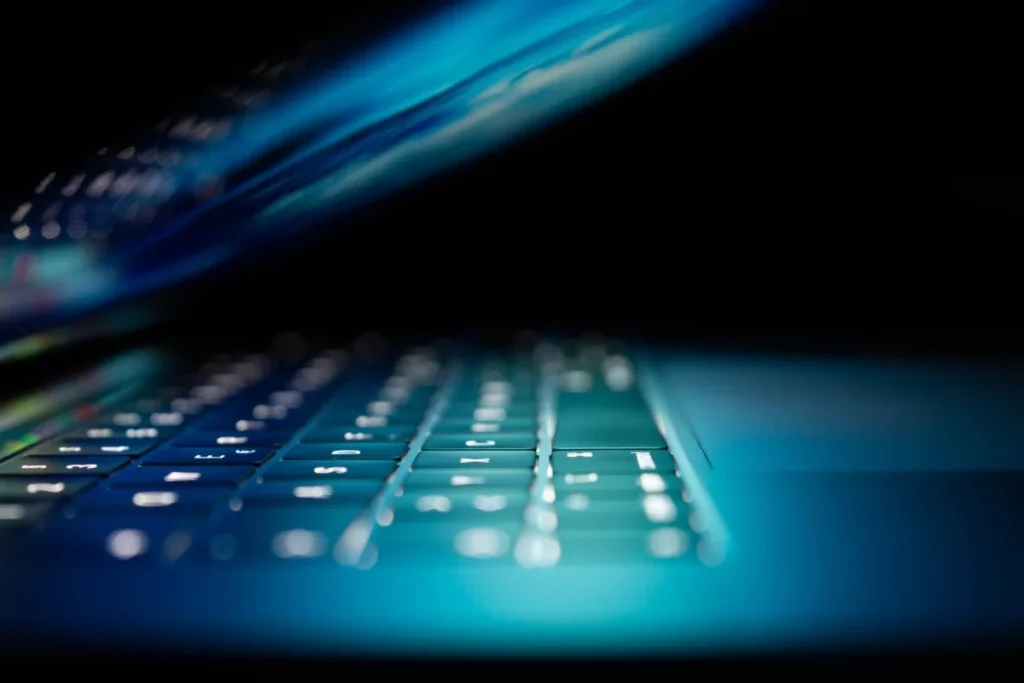Close-up of illuminated laptop keyboard in dark cyber-themed environment.