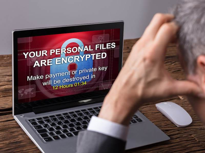 Man staring at laptop screen with ransomware encryption warning message.