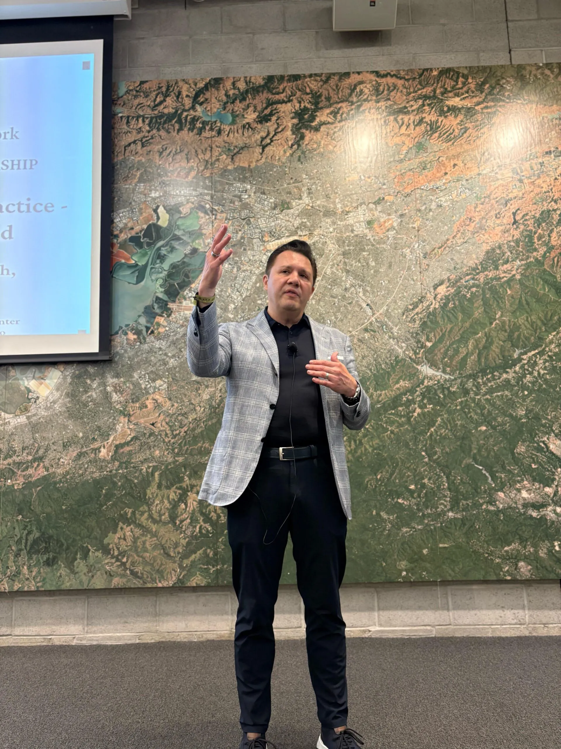 Professional speaker presenting in front of geographic data map and projection screen.